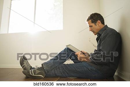 Hispanic man using digital tablet on floor of empty room View Large Photo Image Stock Photograph - Hispanic man using digital tablet on floor of empty room. Fotosearch