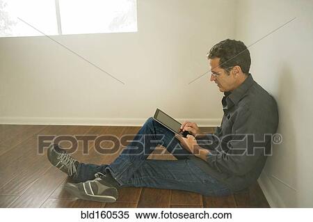 Stock Photography - Hispanic man using digital tablet on floor of empty room. Fotosearch