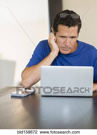 Stock Image - Hispanic man using laptop at table. Fotosearch