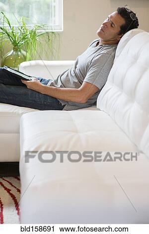Stock Image - Hispanic man with digital tablet napping on sofa. Fotosearch