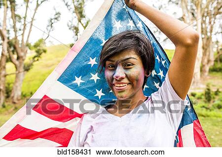 Stock Image - Hispanic woman covered in pigment powder holding American flag. Fotosearch