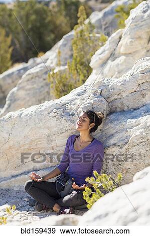 Stock Photo - Hispanic woman meditating on rocky hillside. Fotosearch