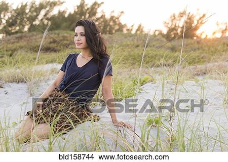 Picture - Hispanic woman sitting on sand dunes. Fotosearch