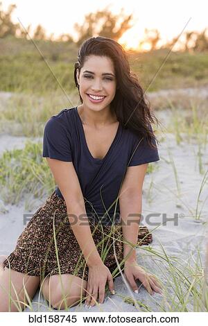 Stock Photography - Hispanic woman sitting on sand dunes. Fotosearch
