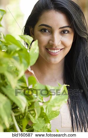 Hispanic woman smiling behind plant View Large Photo Image Stock Photo - Hispanic woman smiling behind plant. Fotosearch