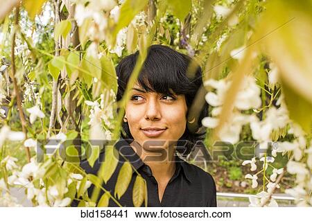 Stock Image - Hispanic woman smiling in foliage. Fotosearch