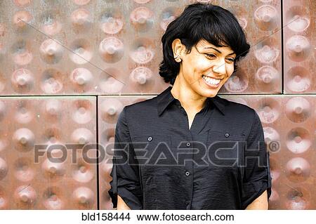 Picture - Hispanic woman smiling near metal wall. Fotosearch