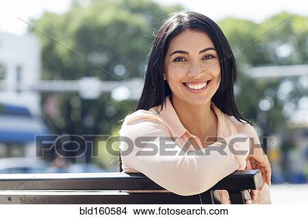 Picture - Hispanic woman smiling on bench. Fotosearch