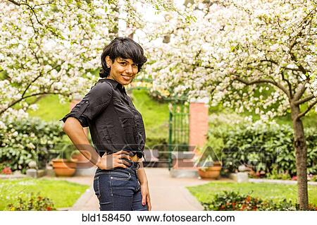 Stock Image - Hispanic woman smiling under flowering trees. Fotosearch