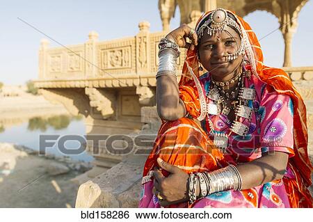 Stock Photograph - Indian woman wearing traditional jewelry sitting near monument, Jaisalmer, Rajasthan, India. Fotosearch