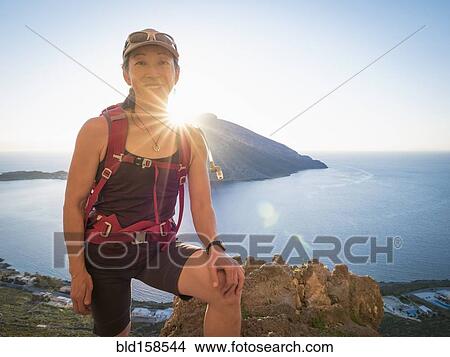 Picture - Japanese hiker standing on hilltop over ocean. Fotosearch