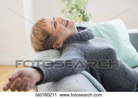 Stock Image - Laughing Caucasian woman laying on sofa. Fotosearch