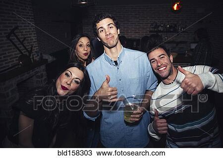 Stock Image - Laughing friends giving thumbs up in nightclub. Fotosearch