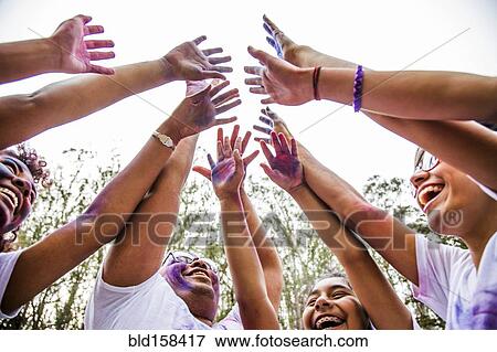 Stock Photo - Low angle view of friends covered in pigment powder cheering. Fotosearch