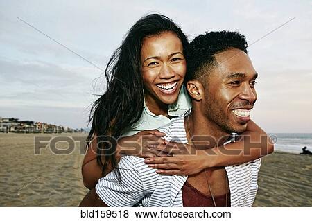 Man carrying girlfriend piggyback on beach View Large Photo Image Stock Photo - Man carrying girlfriend piggyback on beach. Fotosearch
