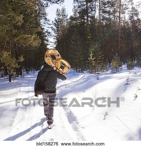 Stock Photograph - Mari man carrying snowshoes on snowy path. Fotosearch