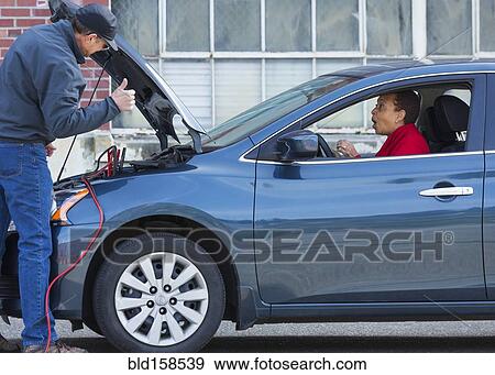 Stock Photo - Mechanic jumping battery for woman in car. Fotosearch