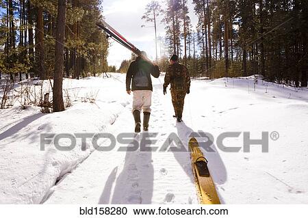 Stock Image - Men carrying skis on snowy path. Fotosearch