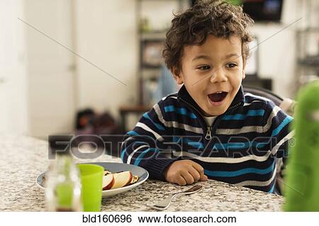 Stock Photograph - Mixed race boy eating at kitchen counter. Fotosearch
