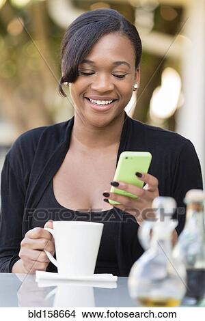 Picture - Mixed race businesswoman using cell phone at outdoor cafe. Fotosearch