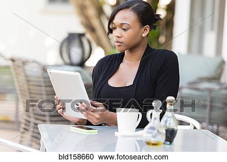 Stock Image - Mixed race businesswoman using digital tablet at outdoor cafe. Fotosearch