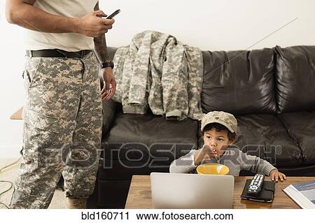 Stock Image - Mixed race father soldier and son relaxing in living room. Fotosearch