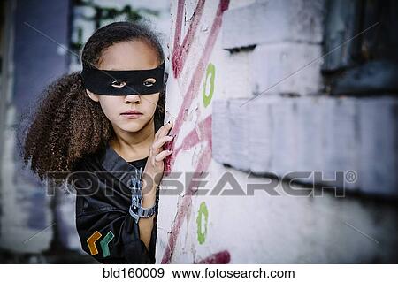 Stock Photo - Mixed race girl in mask peeking around corner. Fotosearch