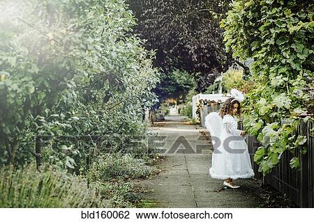 Stock Image - Mixed race girl wearing angel costume on sidewalk. Fotosearch