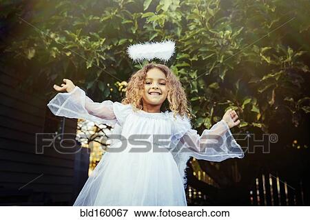 Stock Photo - Mixed race girl wearing angel costume in backyard. Fotosearch