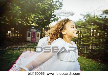 Stock Photograph - Mixed race girl wearing angel costume in backyard. Fotosearch