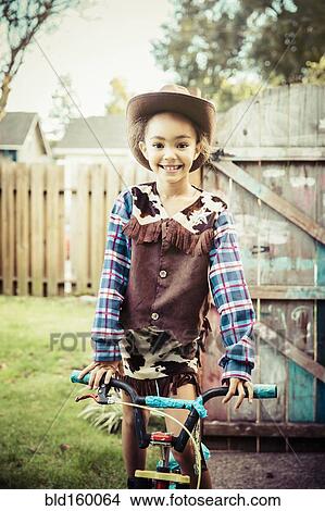 Picture - Mixed race girl wearing cowboy costume in backyard. Fotosearch