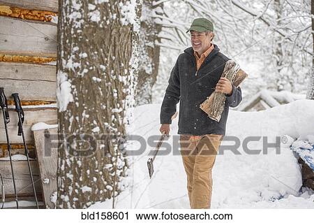 Stock Image - Mixed race man carrying firewood in snow. Fotosearch