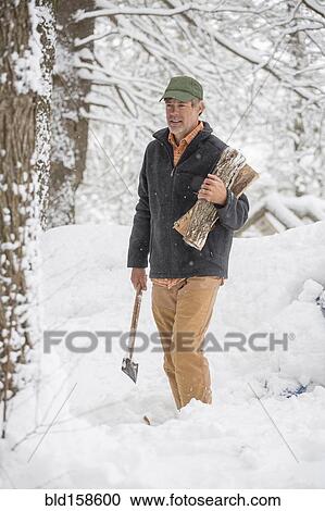 Stock Image - Mixed race man carrying firewood in snowy forest. Fotosearch