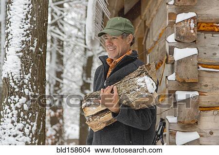 Picture - Mixed race man carrying firewood near snowy shed. Fotosearch