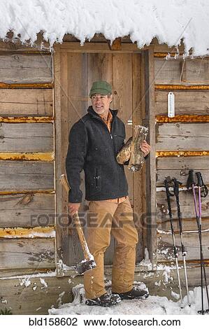 Stock Image - Mixed race man carrying firewood near snowy shed. Fotosearch