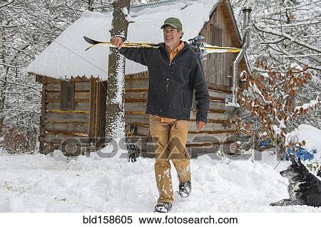 Stock Photography - Mixed race man carrying skis near snowy shed. Fotosearch
