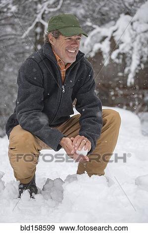Stock Photo - Mixed race man making snowballs in snow. Fotosearch