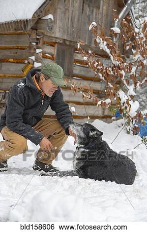 Stock Photograph - Mixed race man petting dog in snow. Fotosearch