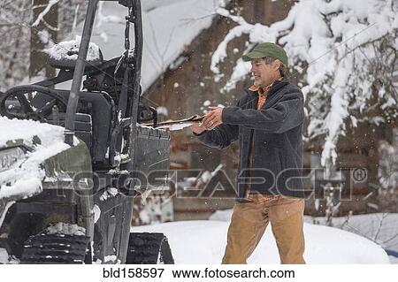 Stock Photo - Mixed race man standing near snow vehicle. Fotosearch