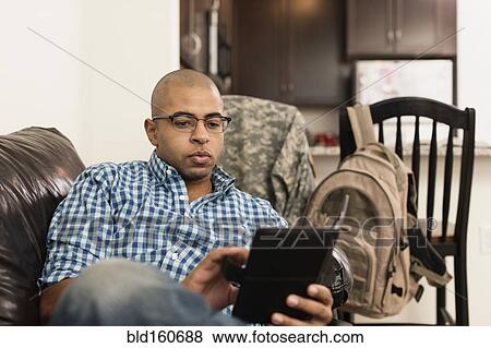 Stock Photo - Mixed race man using digital tablet on sofa in living room. Fotosearch