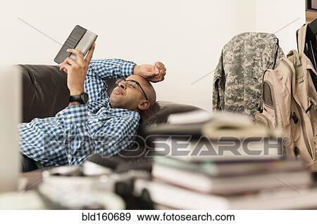 Stock Photo - Mixed race man using digital tablet on sofa near books. Fotosearch
