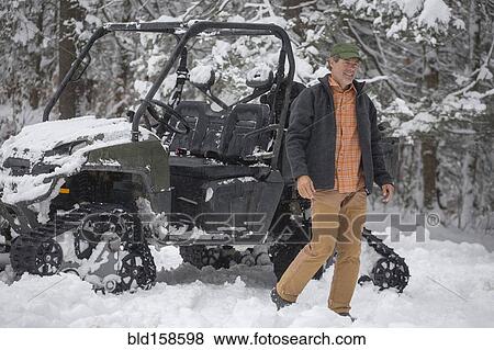 Stock Photo - Mixed race man walking near snow vehicle in snow. Fotosearch