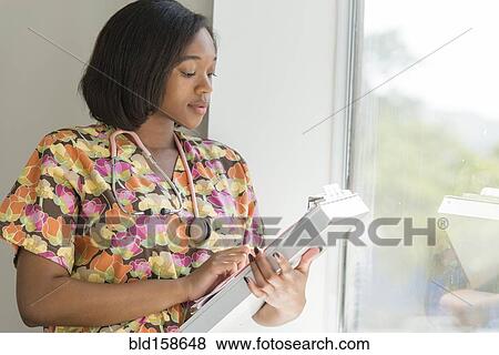 Stock Photo - Mixed race nurse reading medical chart near window. Fotosearch