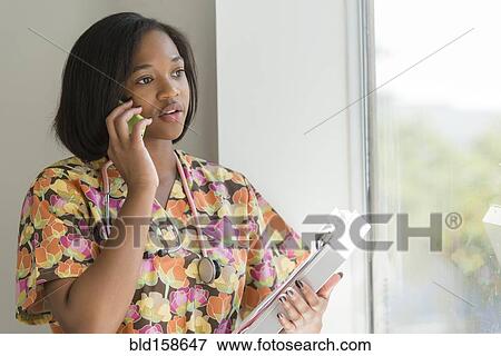 Stock Photo - Mixed race nurse talking on cell phone near window. Fotosearch