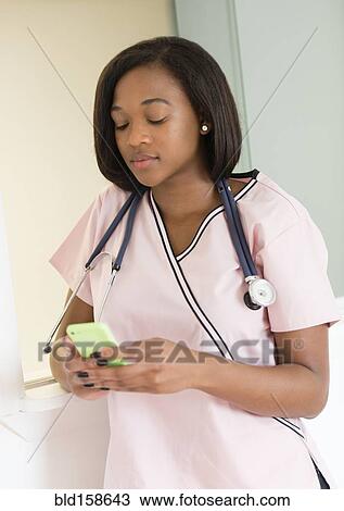Stock Image - Mixed race nurse using cell phone. Fotosearch