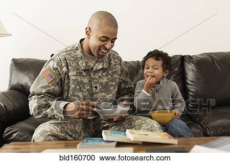 Stock Image - Mixed race soldier father and son from bowls on sofa. Fotosearch