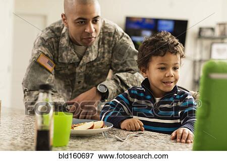 Stock Photo - Mixed race soldier father and son eating in kitchen. Fotosearch