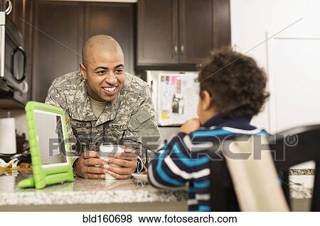 Stock Photo - Mixed race soldier father and son eating in kitchen. Fotosearch