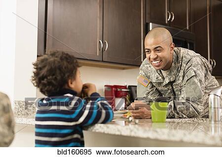 Stock Photography - Mixed race soldier father and son eating in kitchen. Fotosearch