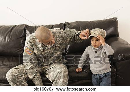 Stock Photo - Mixed race soldier father putting cap on son. Fotosearch